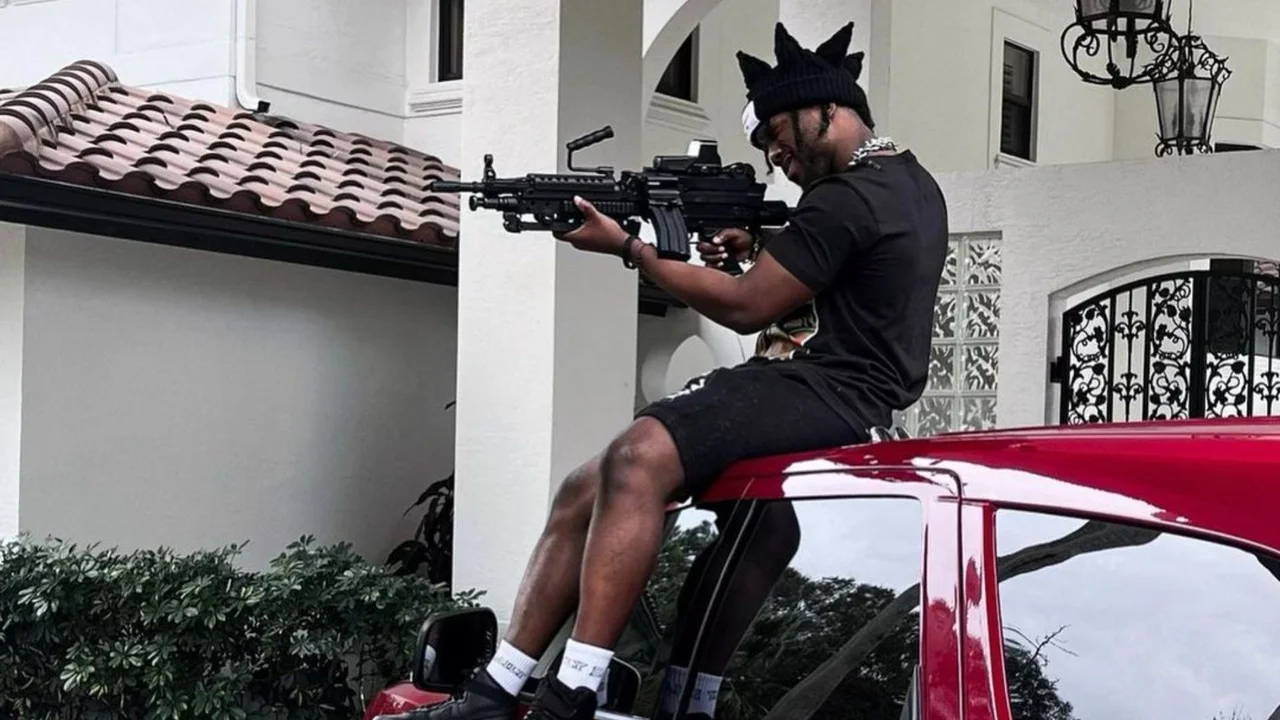 YourRage posing with a gun atop a car
